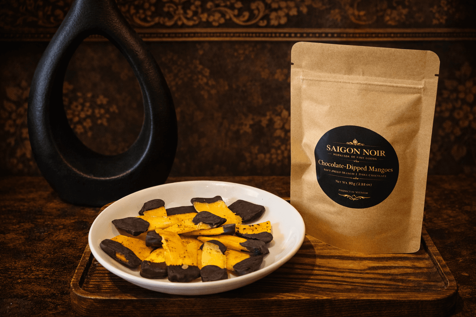 Chocolate-dipped mango on a plate beside a pouch and decorative vase
